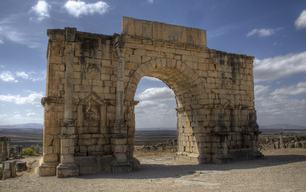 Arch of Caracalla – Volubilis – Morocco – Wikipedia Commons by Prioryman – 1200px-Volubilis_Arch_of_Caracalla_looking_southwest